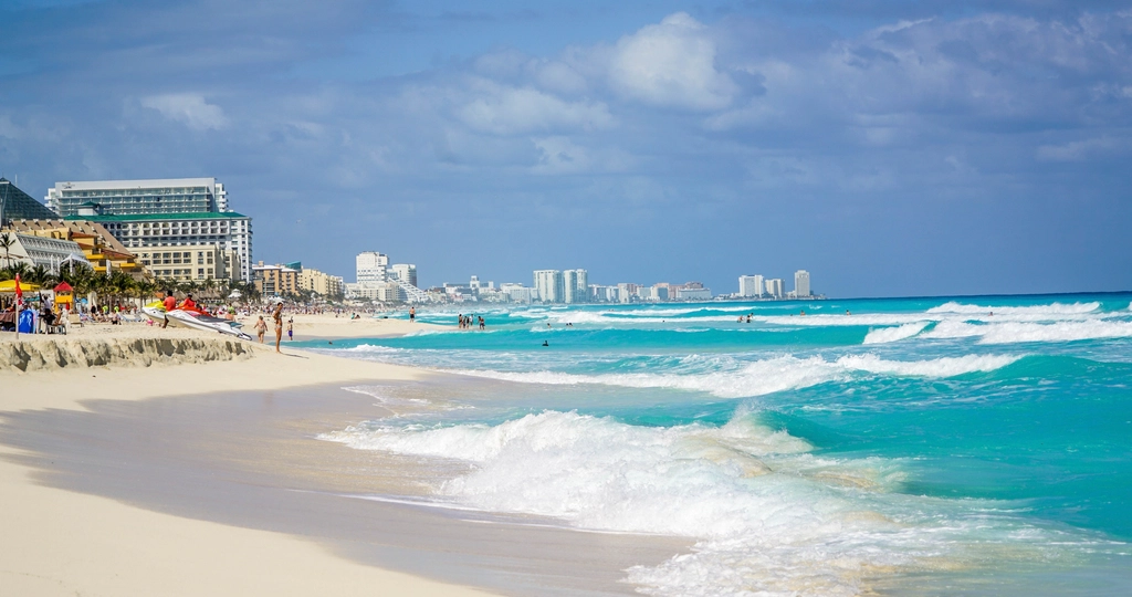 Waves breaking on a wide white-sand beach with resort towers along the shore