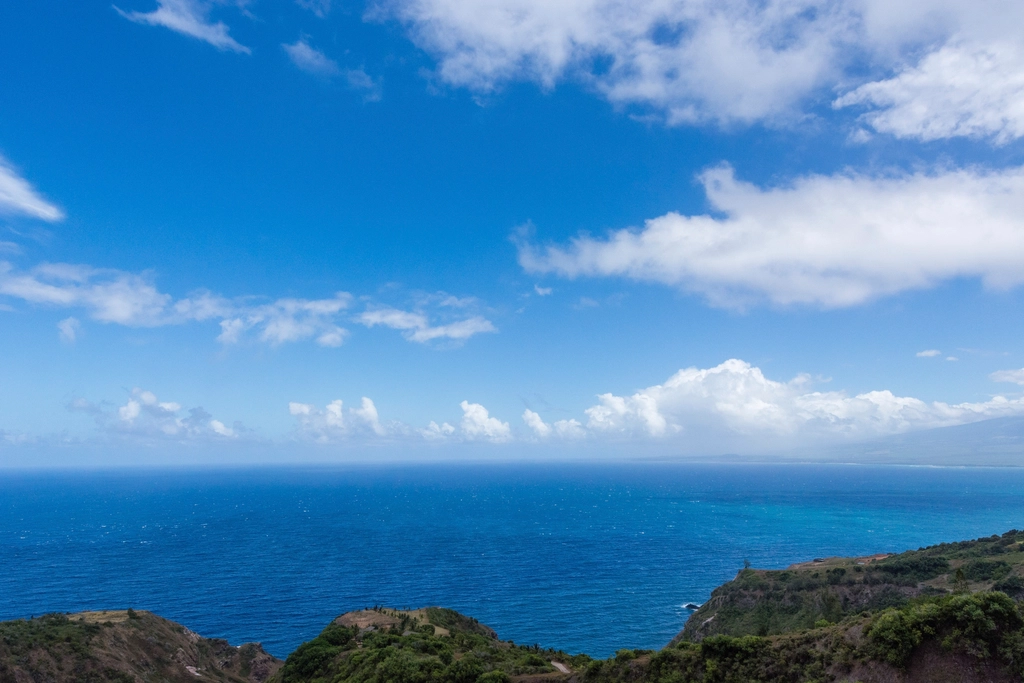 Deep blue ocean seen from a green headland under tall clouds